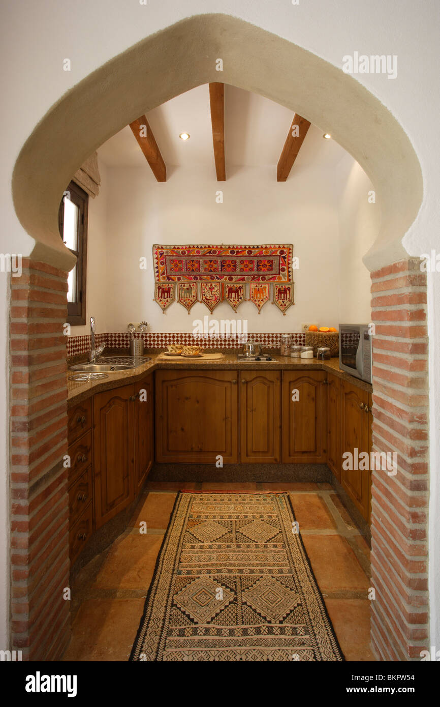 Vista a través del arco de estilo marroquí con pequeña cocina española con unidades de madera y alfombras orientales sobre el piso de baldosas Fotografía de stock - Alamy Vista a través del arco de estilo marroquí con pequeña cocina española con unidades de madera y alfombras orientales sobre el piso de baldosas Fotografía de stock - Alamy
