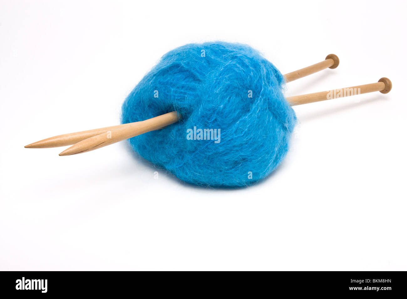 Una gran bola de lana mohair azul perforada con agujas de tejer de madera grande contra blanco. Foto de stock