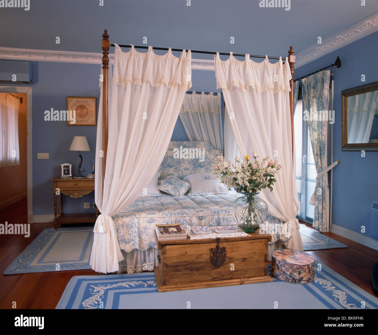 Cortinas blancas en cama con dosel con sábanas blancas+azul en azul pastel  Español dormitorio con pecho grande en madera Fotografía de stock - Alamy