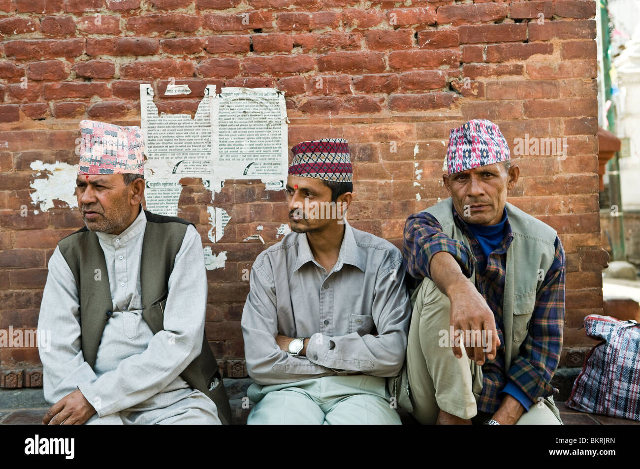 Sentado y viendo a la gente que va por la vida. Nepali hombres vestidos tradicionales sombreros nepalí. Foto de stock