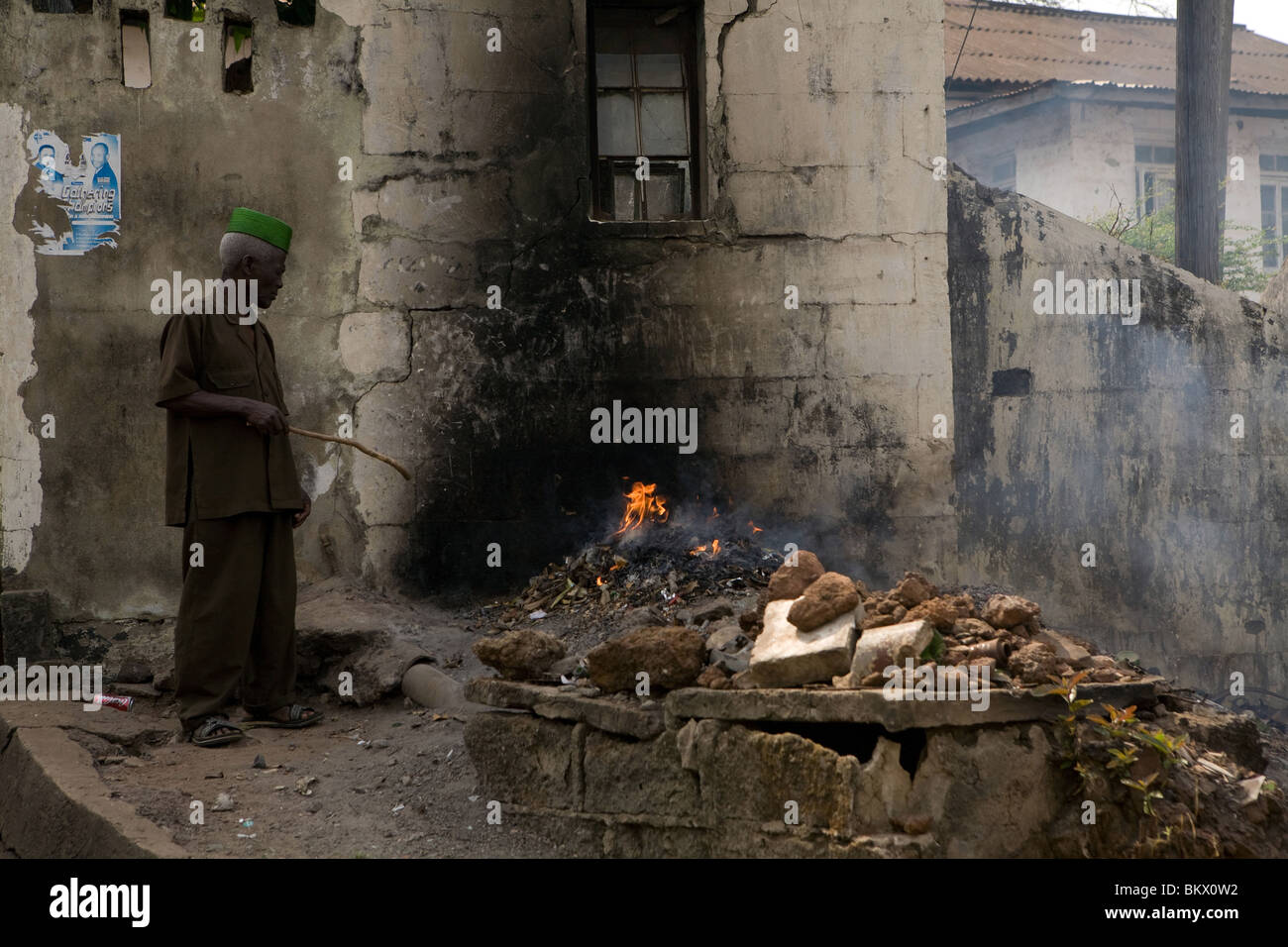 Un hombre se quema de basura quemada en una ruina en Freetown, Sierra Leona Foto de stock