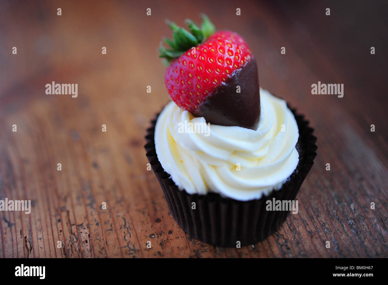 Un cupcake hechas de esponja de Chocolate, coronado con crema y una fresa Foto de stock