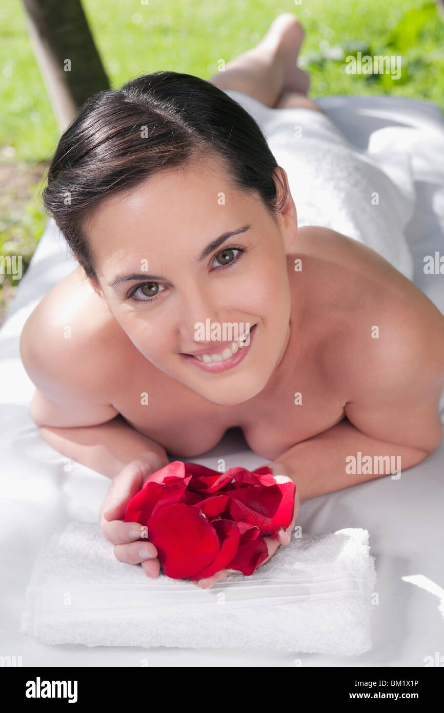 Retrato de una mujer acostada sobre una camilla de masaje, la celebración de pétalos de rosa Foto de stock