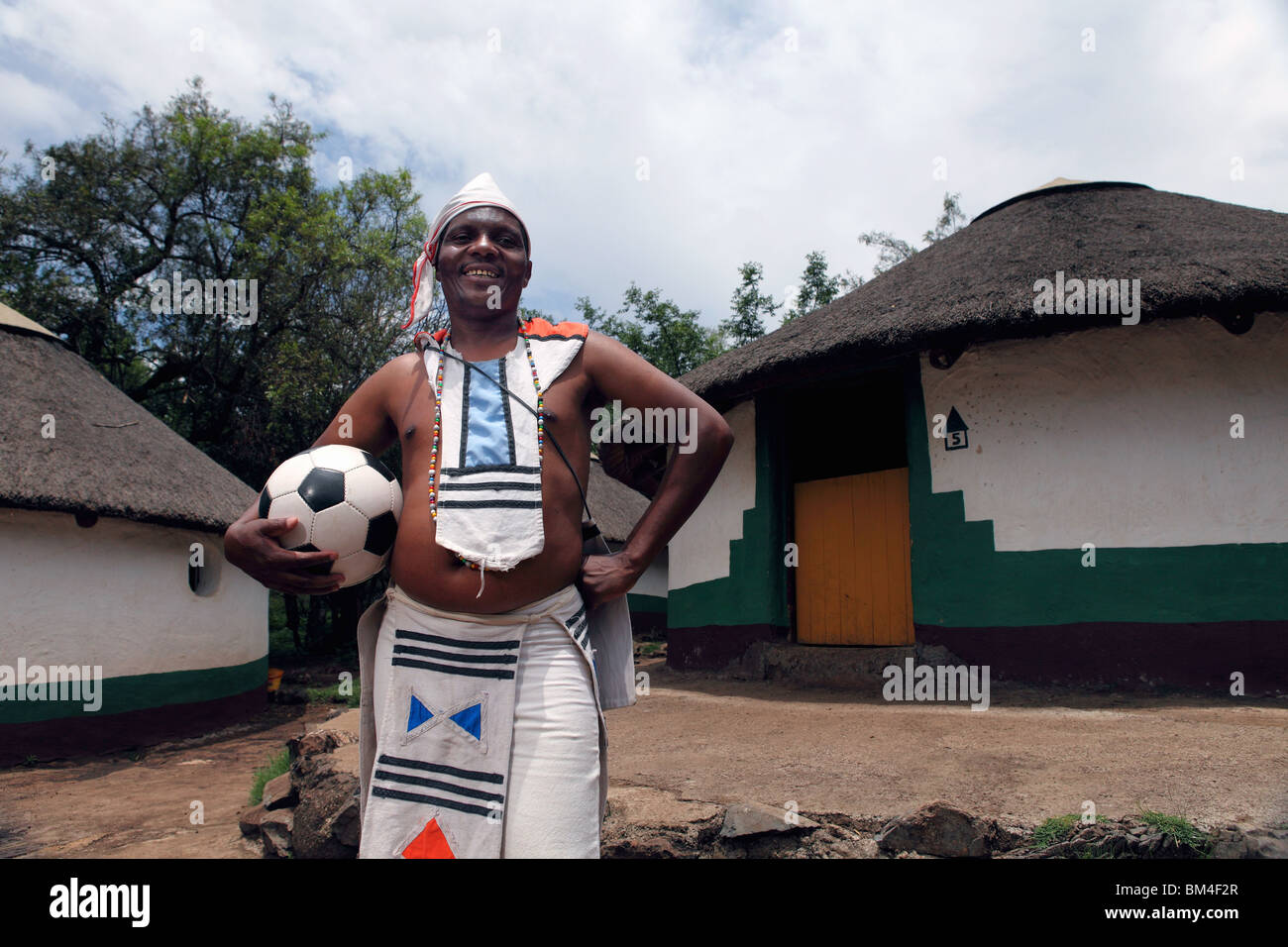 Un hombre de origen tribal Xhosa viste ropas tradicionales mientras posa con un balón de fútbol en un pueblo tradicional en Sudáfrica Foto de stock