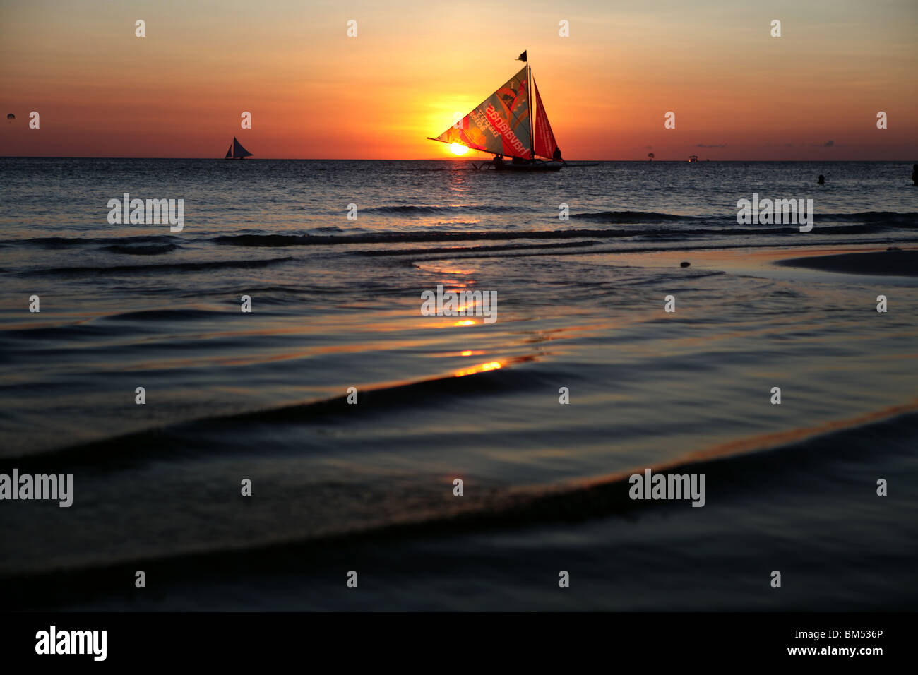 Un bote de vela pasa el atardecer en la Playa Blanca, Boracay, el destino turístico más famoso en Filipinas. Foto de stock