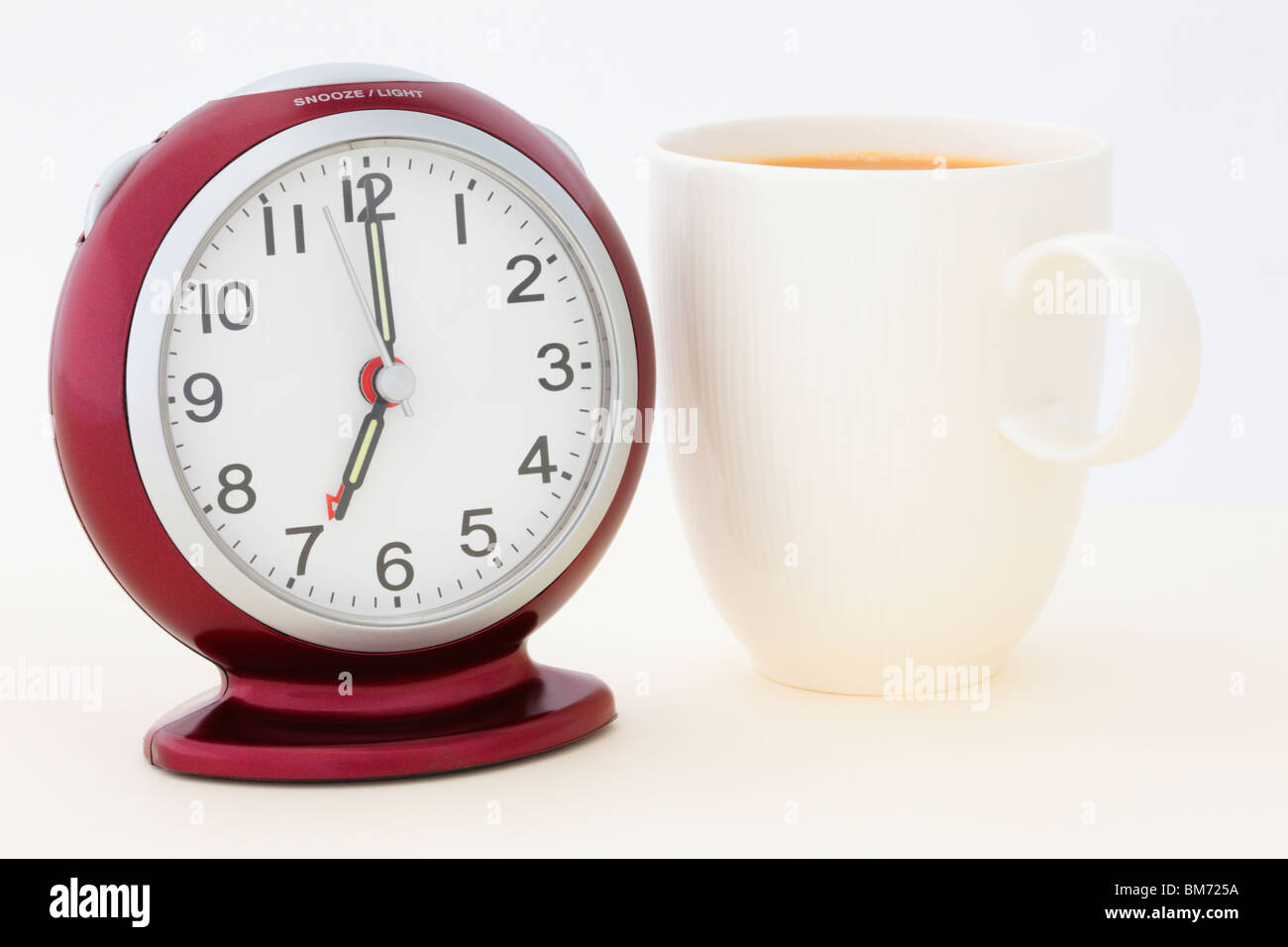 Taza de Té por un despertador rojo a las 7 de la mañana, pocos segundos antes de la alarma suena a la hora de levantarse. Inglaterra Gran Bretaña Foto de stock