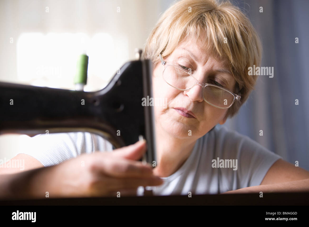 Mujer madura ajusta el pie de máquina de coser Foto de stock