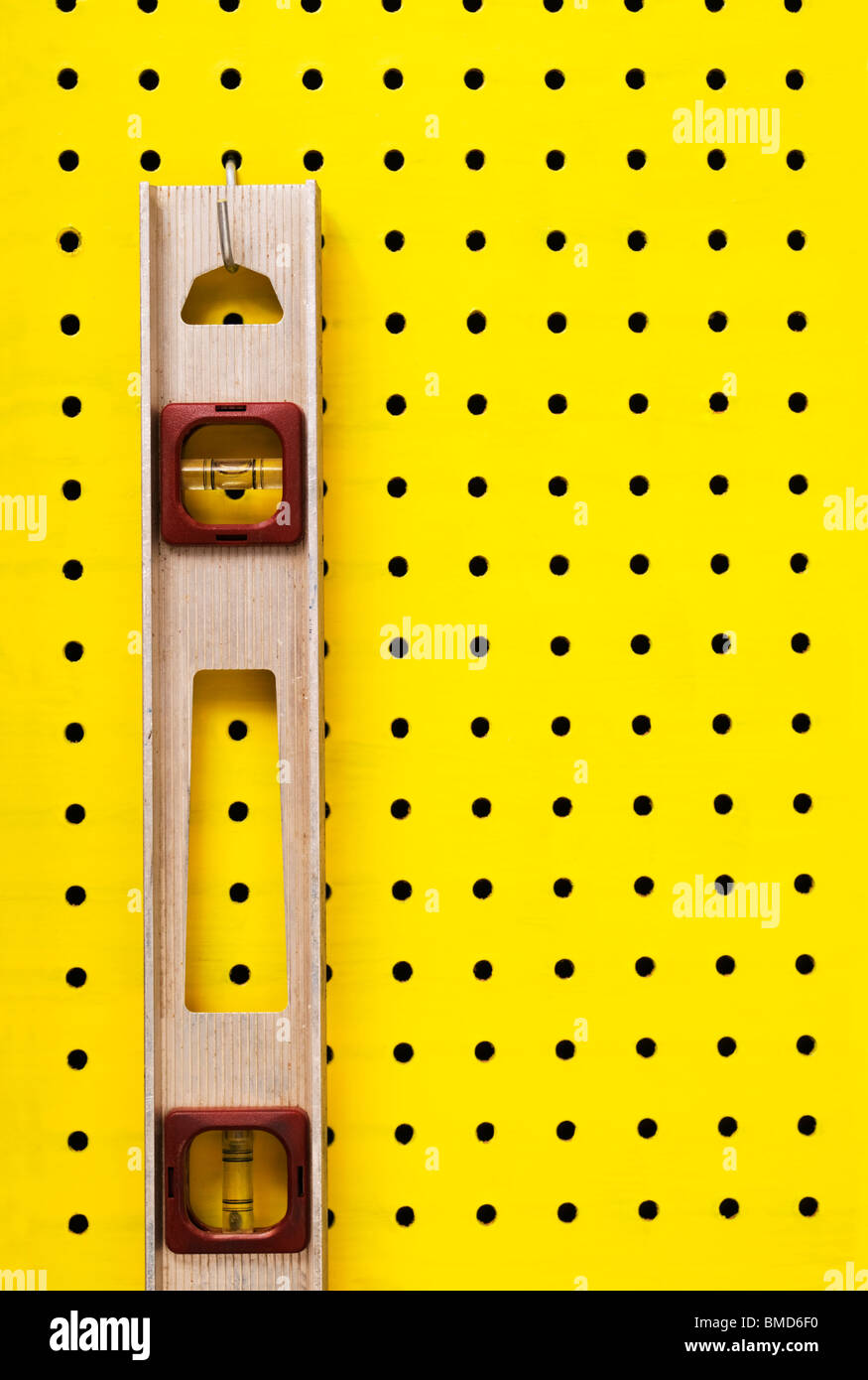Nivel viejo cuelga de un gancho sobre amarillo pegboard. Foto de stock