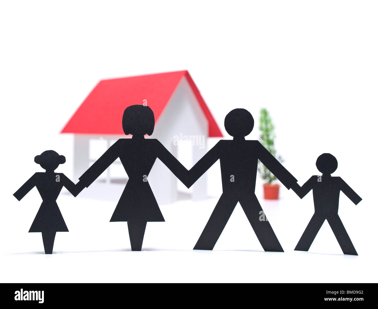 Una familia de papel está manteniendo las manos junto a su nueva casa de papel. Foto de stock