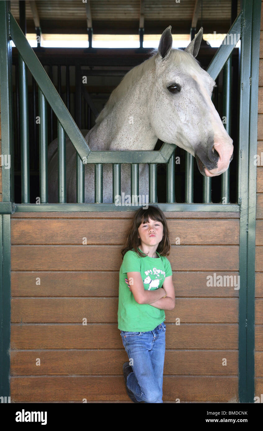 Niña de pie debajo de caballo en el granero Foto de stock