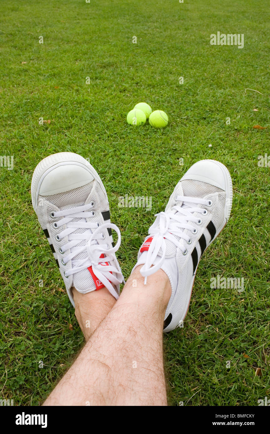 Los pies de un hombre vistiendo un par de blancos de Adidas instructores y  3 pelotas de tenis Fotografía de stock - Alamy