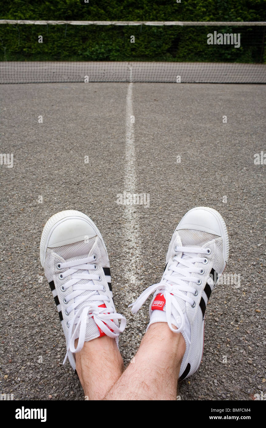 Los pies de un hombre vestidos de blanco Adidas instructores en una cancha  de tenis Fotografía de stock - Alamy