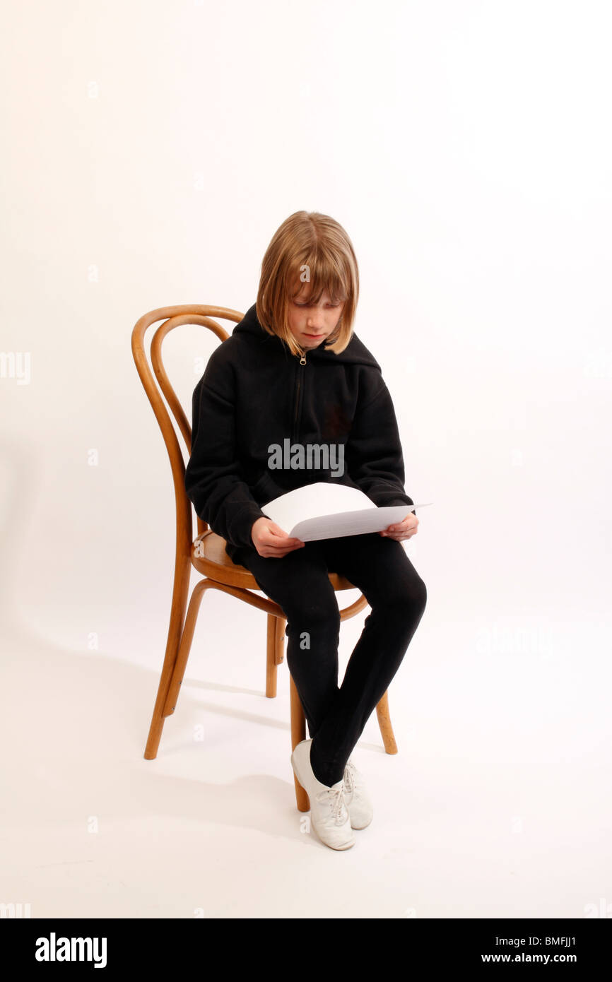 Niño sentado en una silla de madera, vestida de negro, y la lectura de un trozo de papel que muestra los resultados de los exámenes Foto de stock