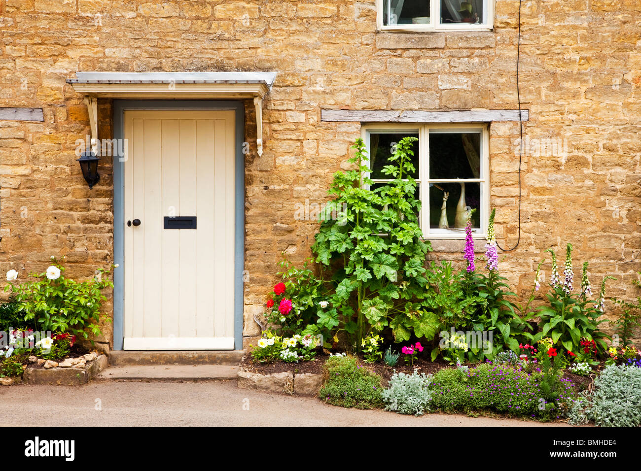 Puerta frontal blanca de una típica casa de pueblo de piedra de Cotswold, con un bonito jardín delantero cottage de flores de verano Foto de stock