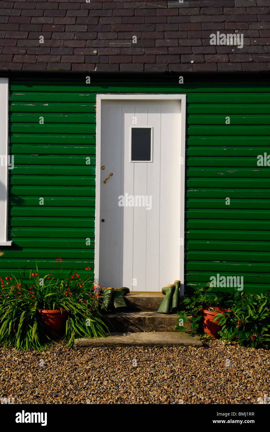 Armstrong Cottages bamburgh revestimiento de madera pintado de verde con wellies en la puerta. Foto de stock