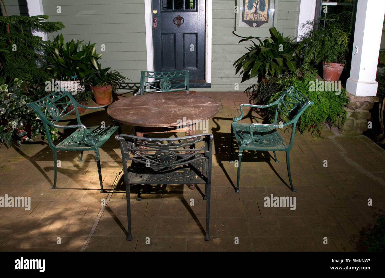 En la veranda cuatro sillas de hierro forjado, una mesa y plantas en macetas. Foto de stock