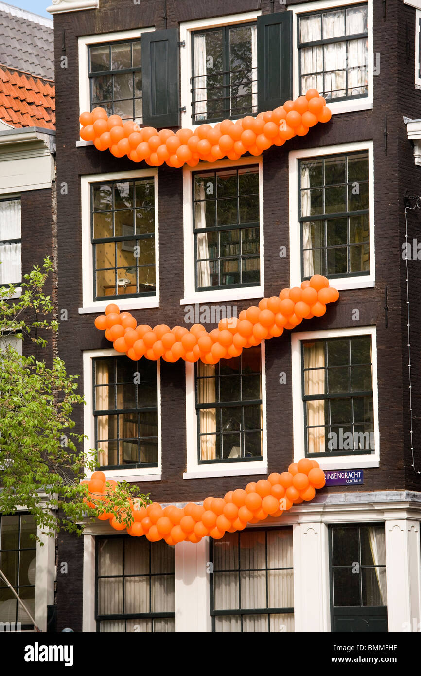 Amsterdam, inclinada canal house en el canal Prinsengracht con guirnaldas de globos naranja sobre Queensday, el cumpleaños de la Reina. Foto de stock