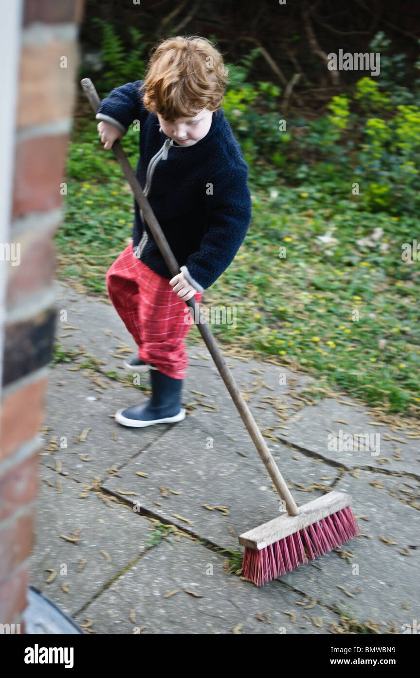 Muchacho barriendo las losas con un cepillo de patio Fotografía de