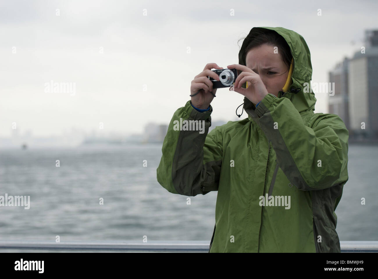 Atourist tomando una fotografía de una excursión en barco por el Río Husdon, Nueva York, EE.UU. en tiempo húmedo vistiendo un impermeable Foto de stock