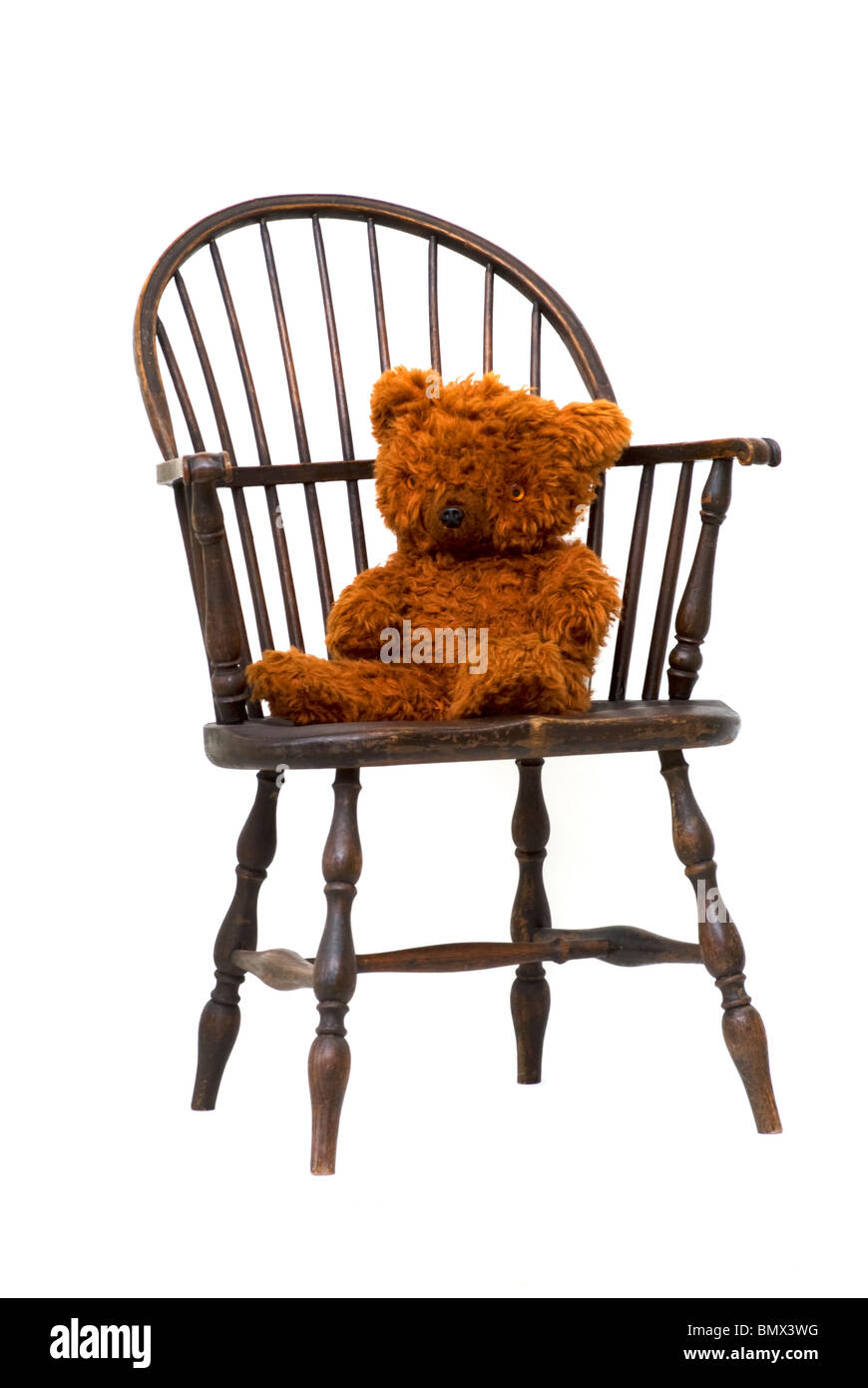 Silla de madera antigua Windsor con osito de peluche marrón vintage sentado en el asiento. La silla está redondeada sin clavos. Foto de stock