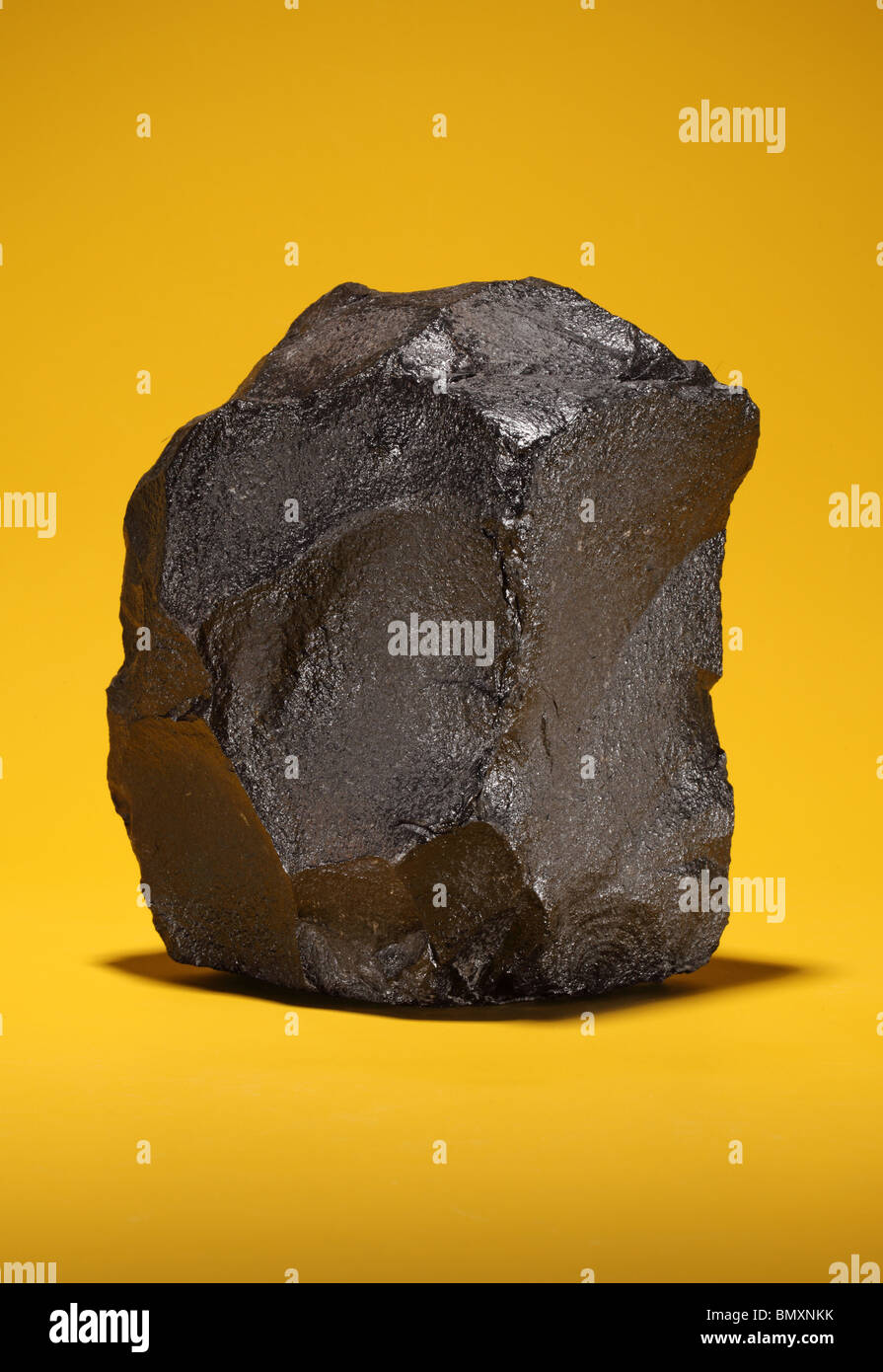 Un gran trozo de carbón bituminoso negro sobre un fondo de color amarillo brillante Foto de stock