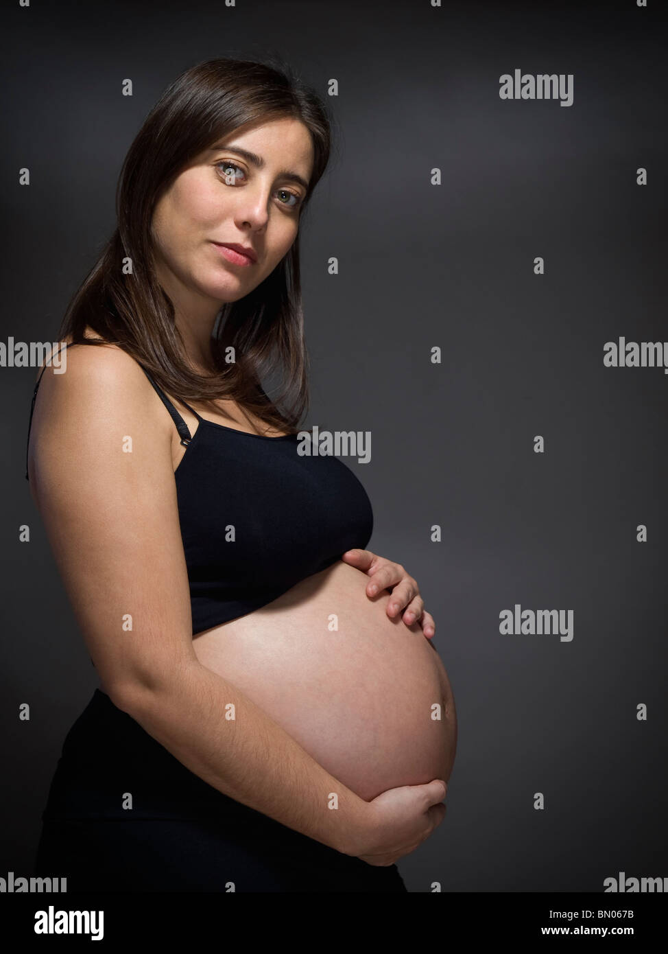Una mujer embarazada tiene su vientre grande sobre un fondo gris. Foto de stock