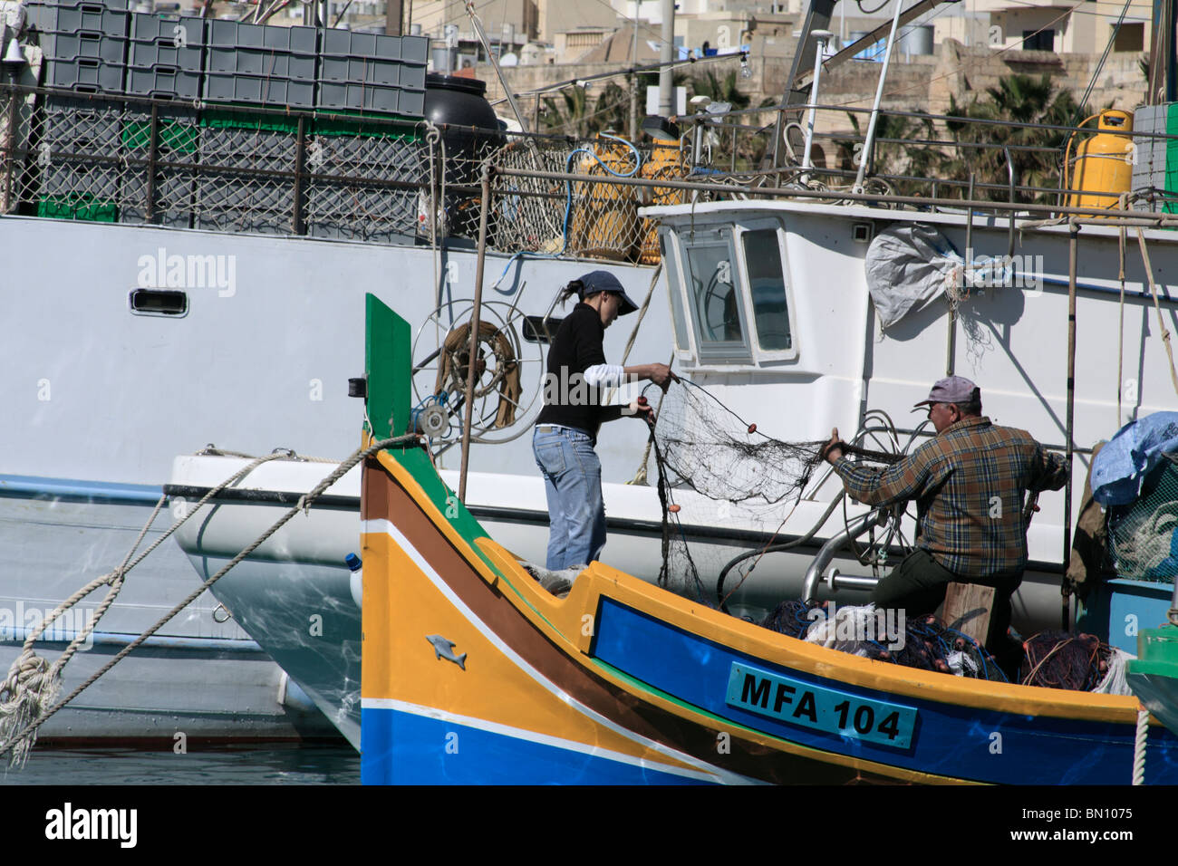 Un padre y su hija preparar sus redes de pesca en una colorida tradicional barco pesquero maltés. Marsaxlokk, Malta Foto de stock