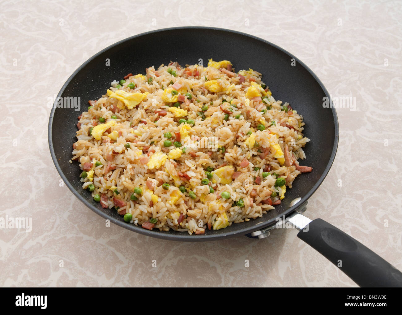 sartén llena de arroz frito con jamón en la mesa Foto de stock