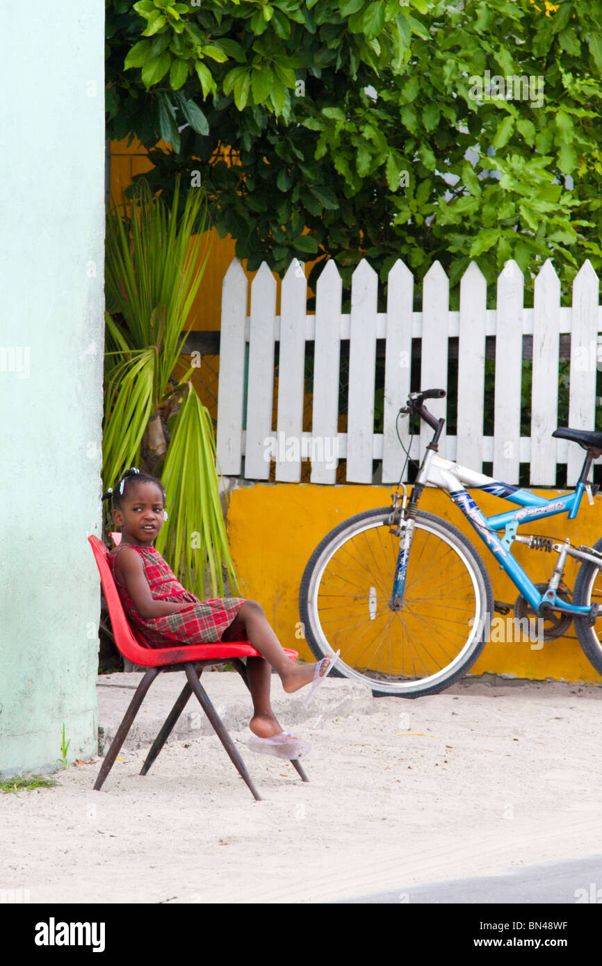 Chica joven se sienta en una silla fuera de su casa en Dunmore street, Harbour Island, Bahamas. Foto de stock