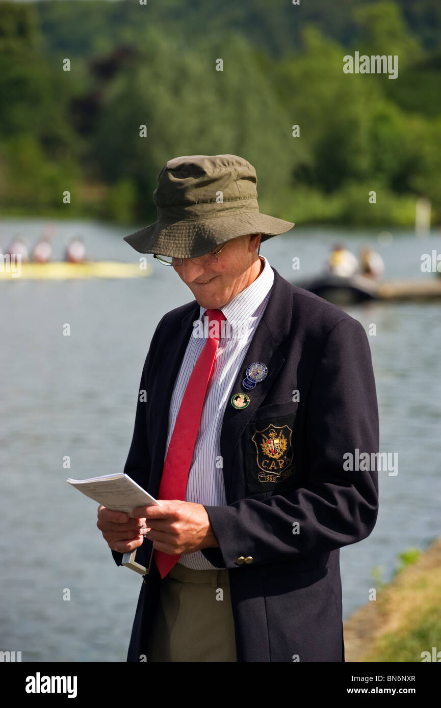 Un hombre vestidos tradicionalmente en chaqueta y corbata portando una insignia Leander Club examina la regata Henley Royal programa. Foto de stock