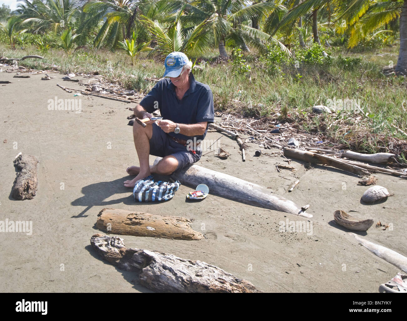 Turista masculino aplanamiento de latas y envases, ayudar a deshacerse de la basura y desperdicios que cubrían esta hermosa playa de Mamitupu. Foto de stock