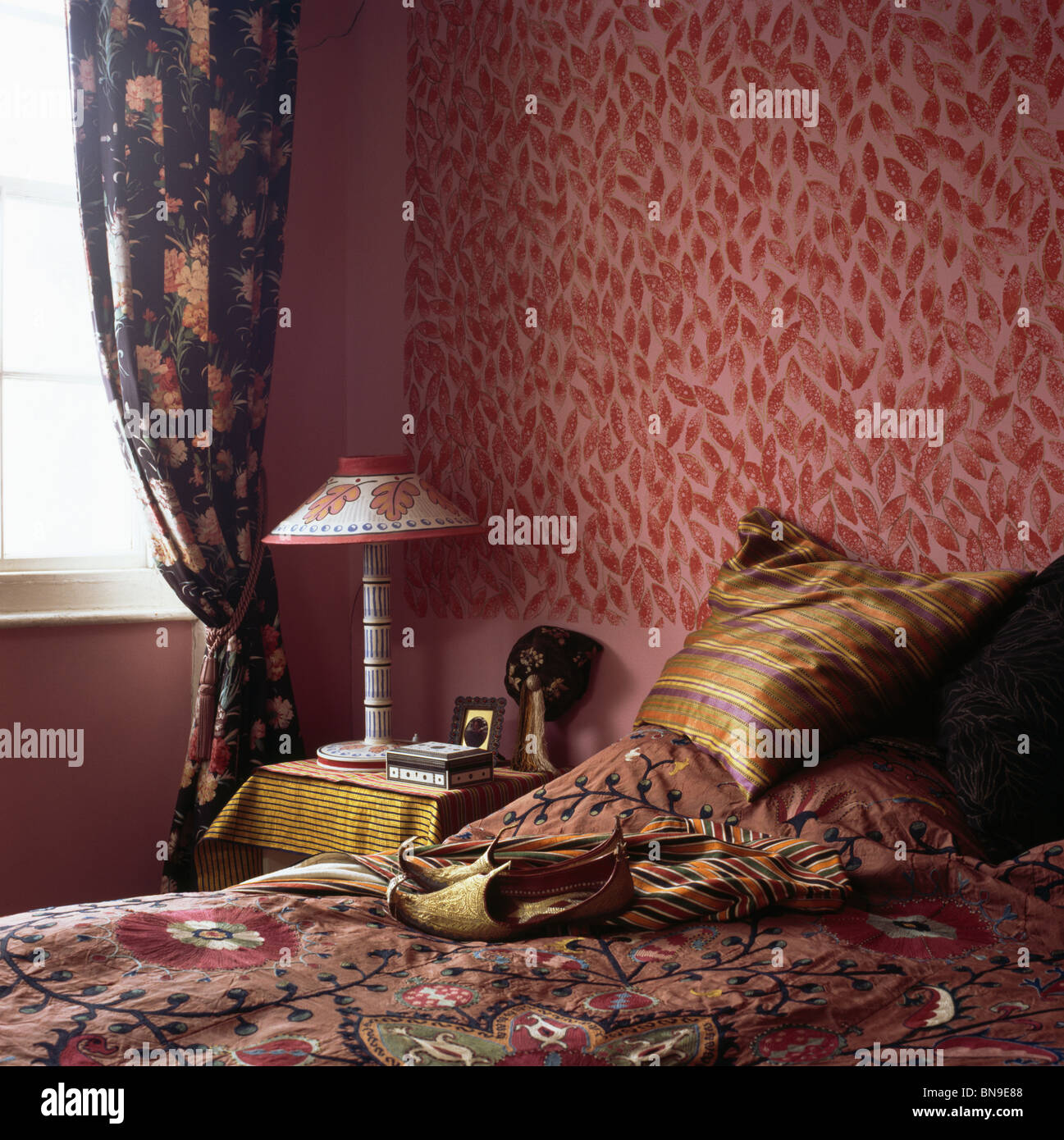 Tapiz rojo estampadas en una habitación pequeña con azul oscuro, cortinas y ropa de cama de colores ricamente diseñado por Cressida Bell Foto de stock