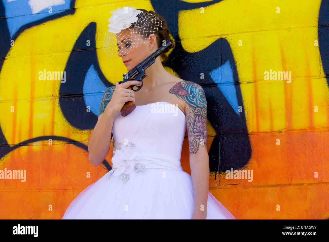 Novia tatuada contra graffitis con pistola de fondo Foto de stock