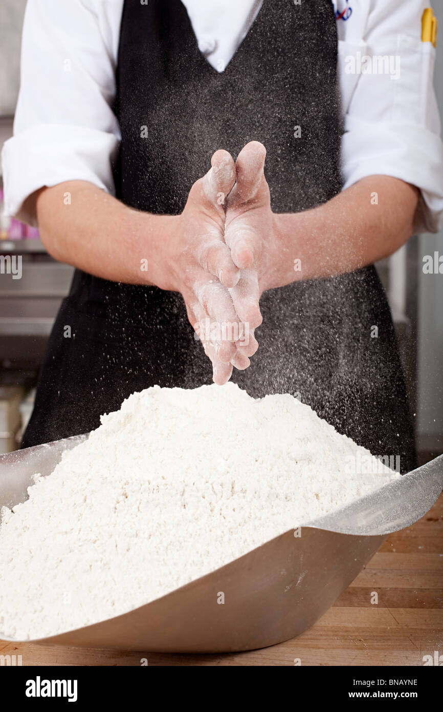 Chef macho roza la harina en las manos en cocina comercial Foto de stock