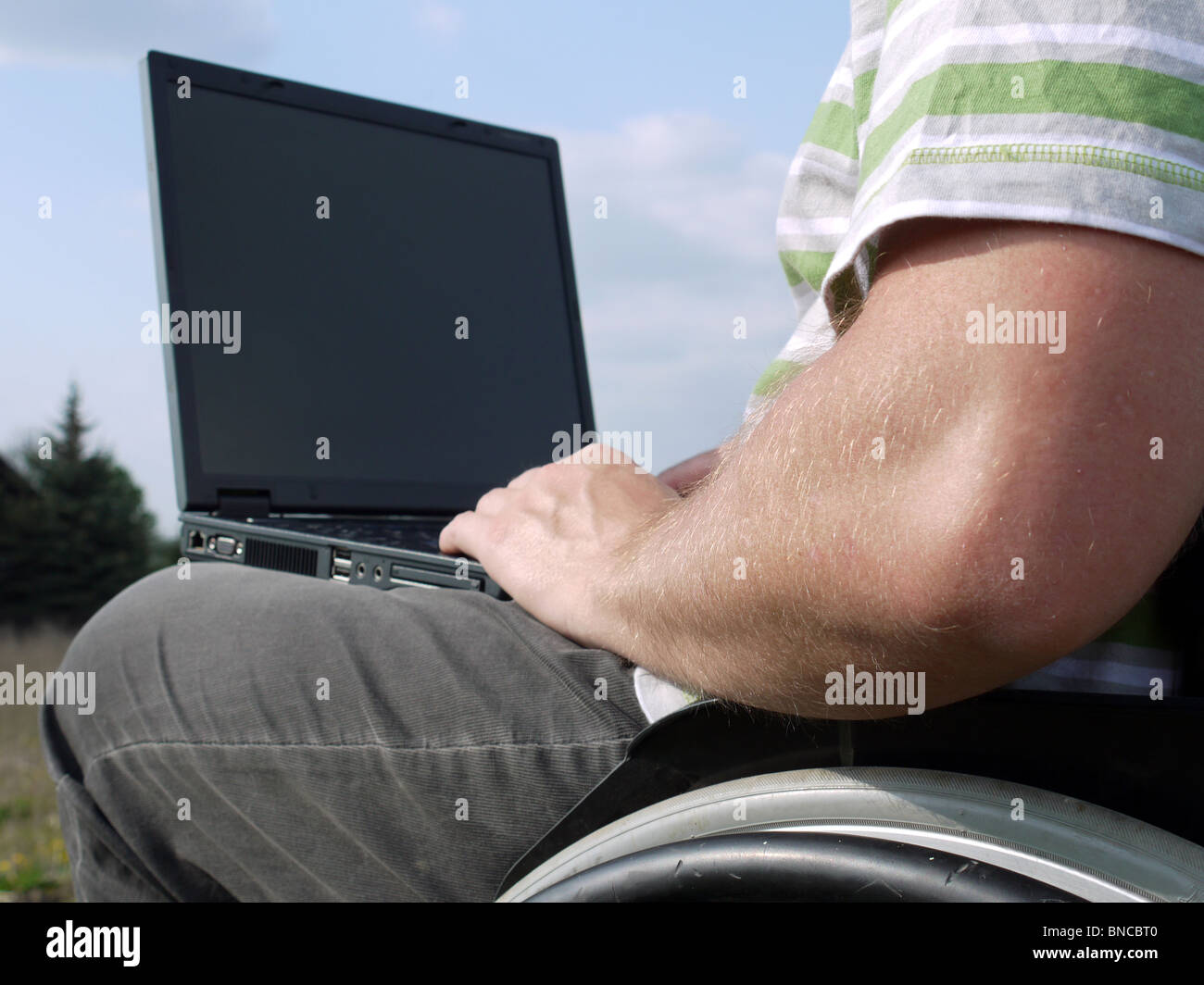 El hombre minusválido en silla de ruedas usando el portátil al aire libre Foto de stock
