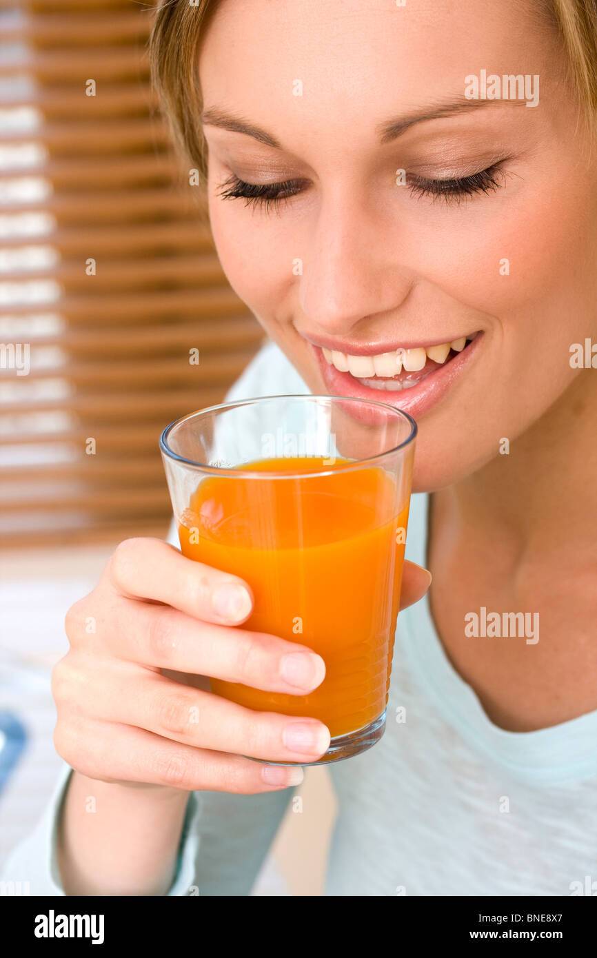Atractiva mujer joven sonriente y tomar jugo de naranja Foto de stock