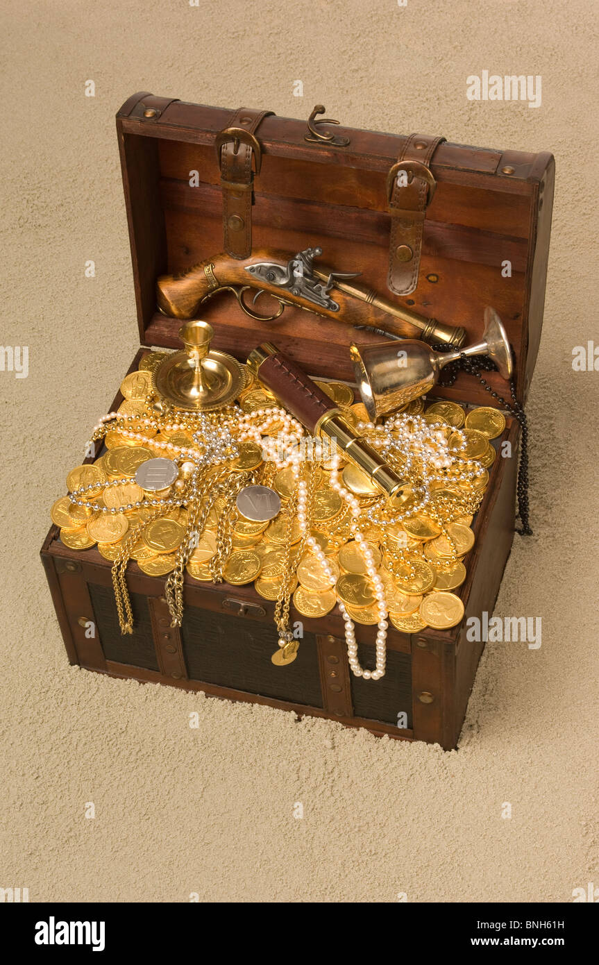 Cofre del tesoro pirata con la tapa abierta rebosante de oro coings y  parafernalia pirata en una playa de arena Fotografía de stock - Alamy