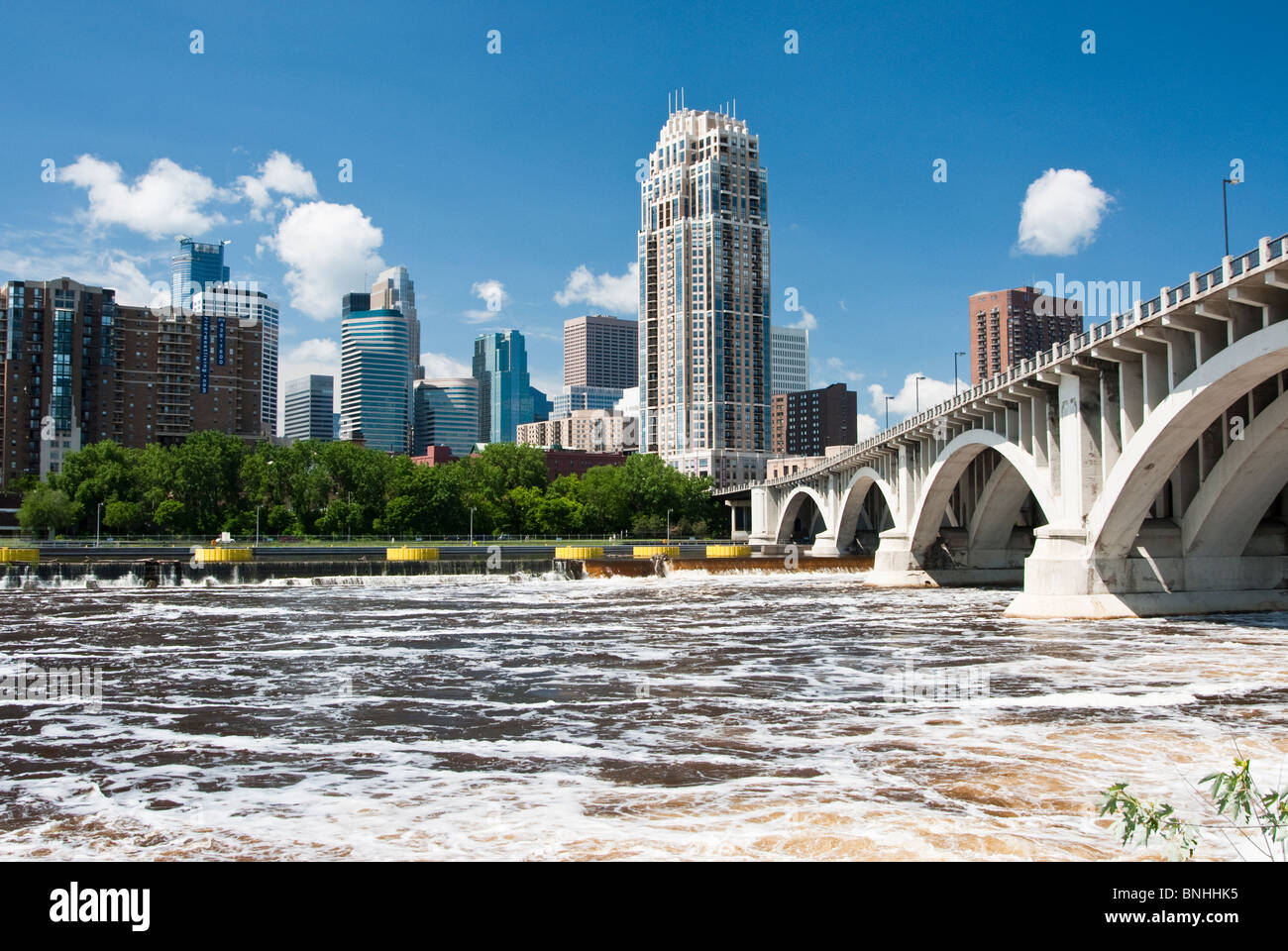 Una vista del horizonte de Minneapolis desde la orilla oeste del Río Mississippi. El río Mississippi es visto en primer plano. Foto de stock