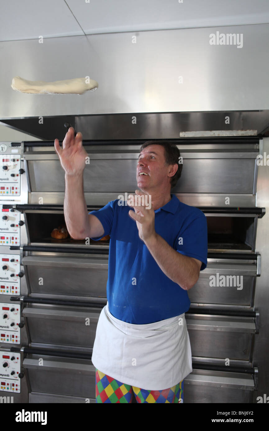 Un panadero se paró delante de un horno de pan arrojar algo de pan de masa  en el aire preparándose para hacer algunos panes o rollos de pan Fotografía  de stock -