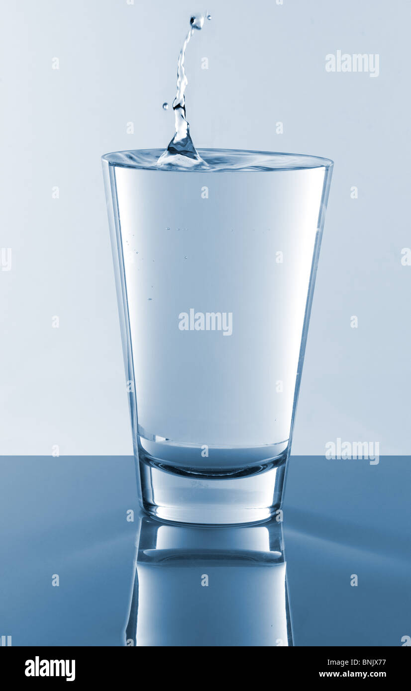 Gota cayendo en un vaso lleno de agua Foto de stock