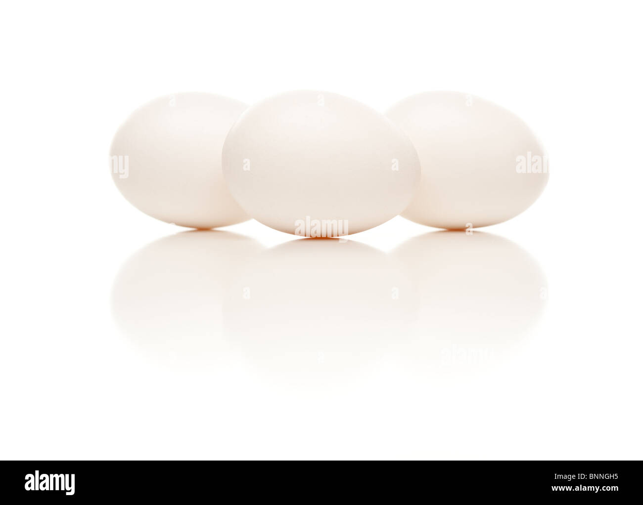 Tres huevos blancos aislados en un fondo blanco reflectante. Foto de stock