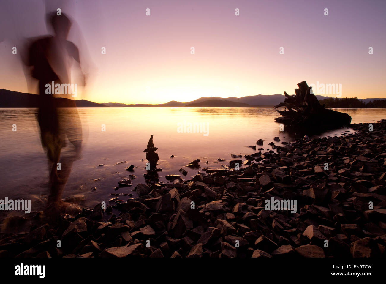 Una figura masculina viendo la puesta de sol sobre el lago y las montañas de Idaho. Foto de stock