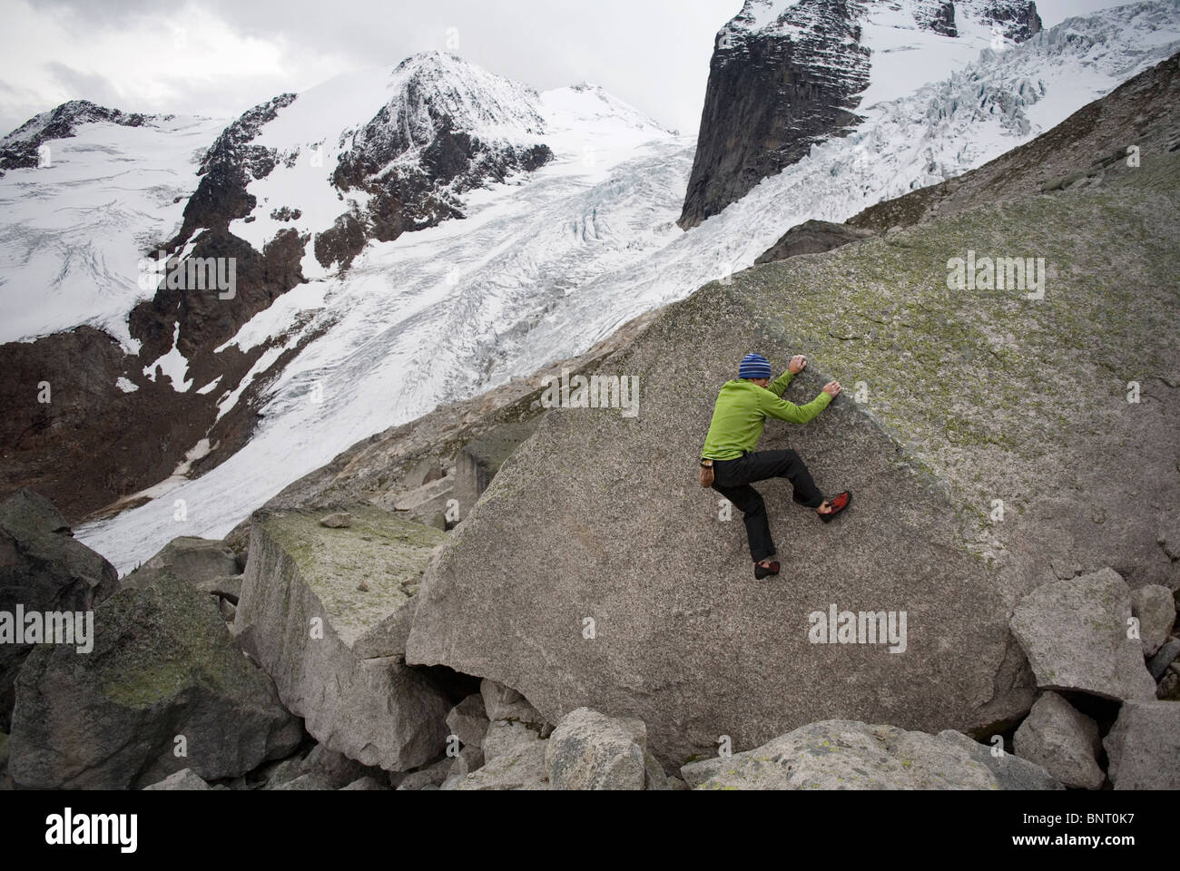 Hombre vestido con una camisa verde trepa a un glaciar con grandes bloques de granito en el fondo. Foto de stock
