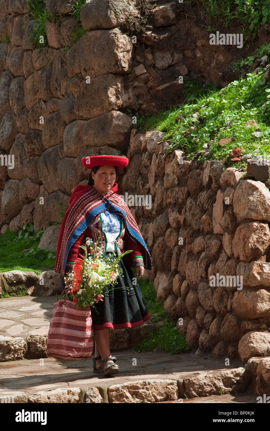 Perú, una mujer lleva a casa un ramo de flores de mercado sobre un camino bordeando un enorme muro de piedra Inca. Foto de stock