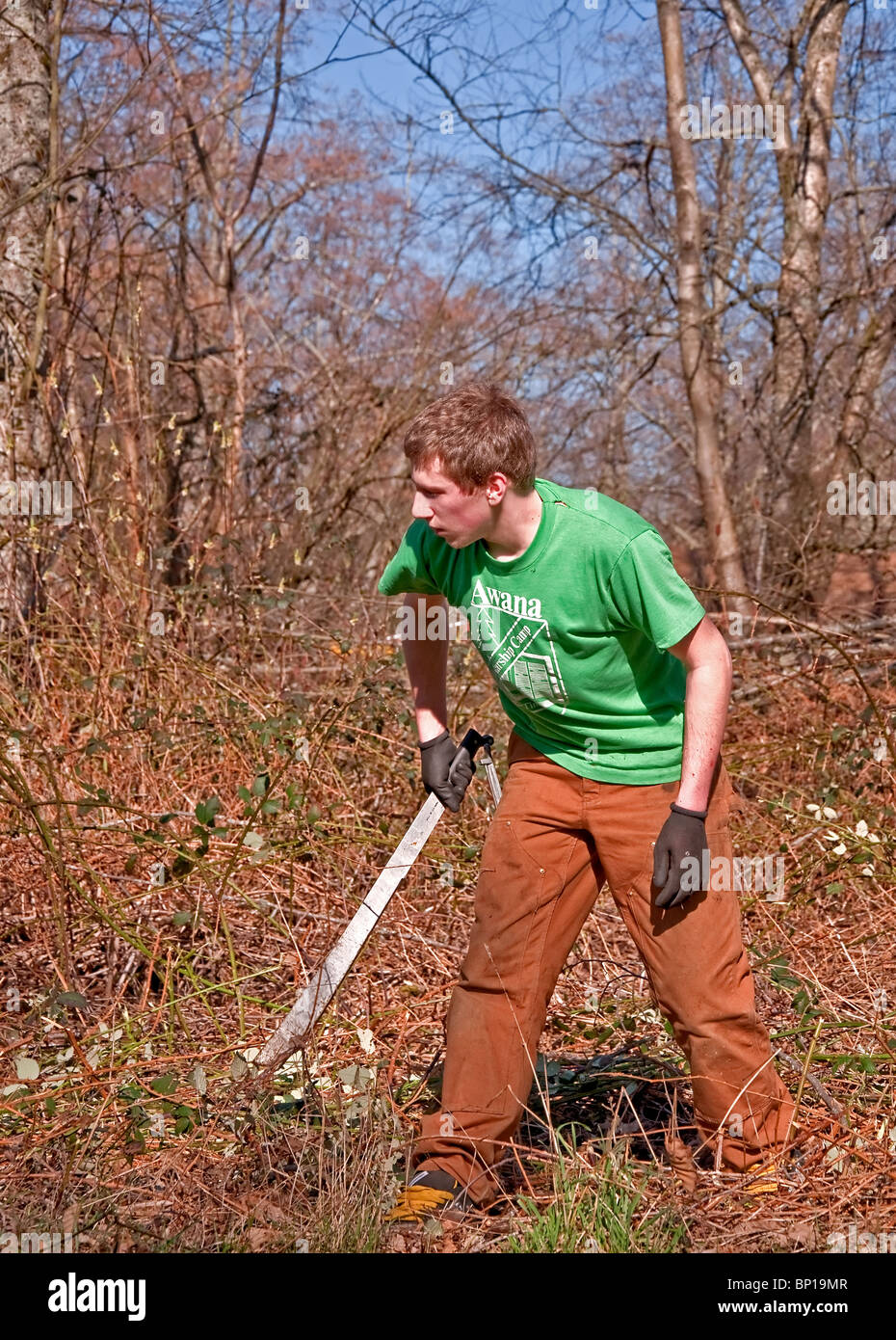 Este joven hombre caucásico en veintitantos años, está trabajando duro para limpiar el cepillo de la tierra con un machete cuchillo. Foto de stock