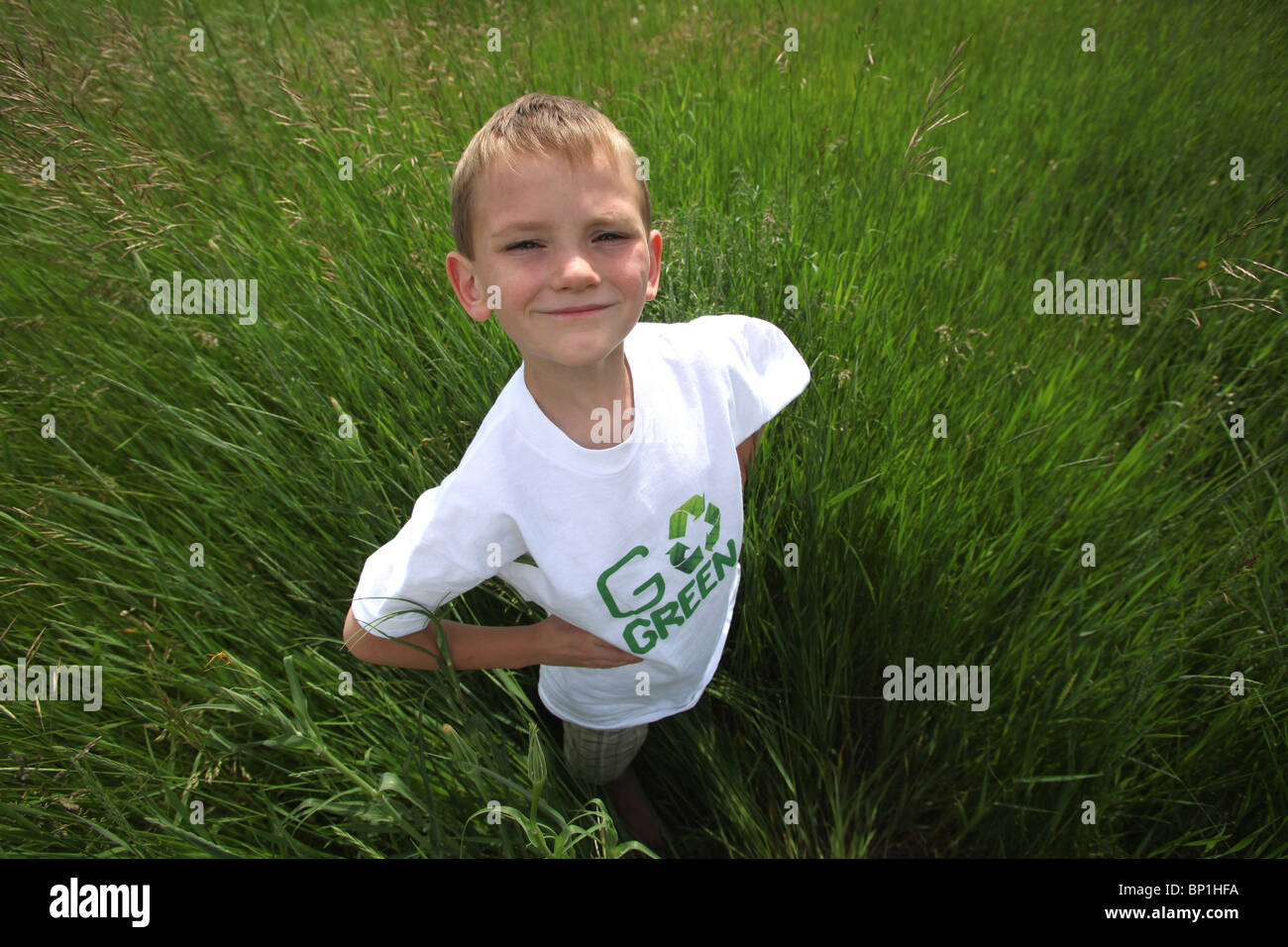 Niño de pie en alto verde césped vistiendo 'Go green' camiseta Foto de stock