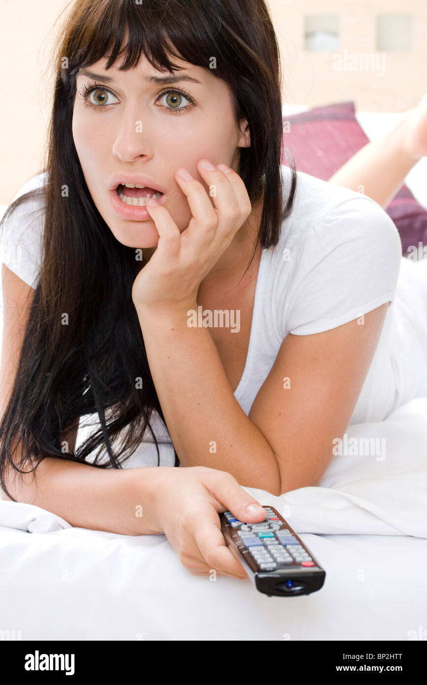 Atractiva mujer joven viendo una película de terror en la televisión solo en una habitación Foto de stock