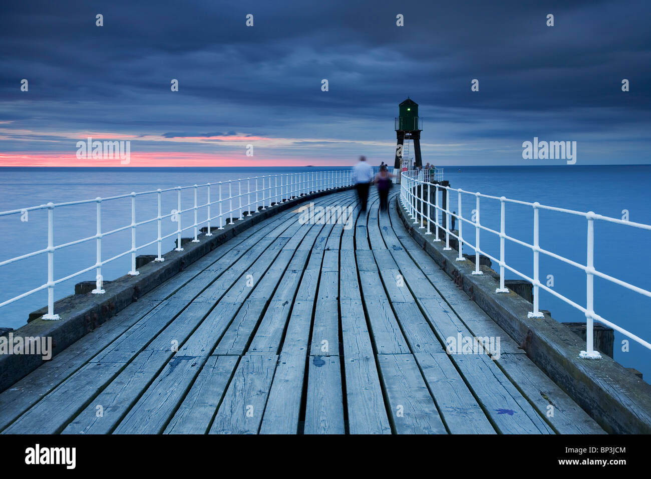 Movimiento borrosos pareja caminando en el muelle al atardecer en Whitby, Whitby, North Yorkshire, Reino Unido Foto de stock