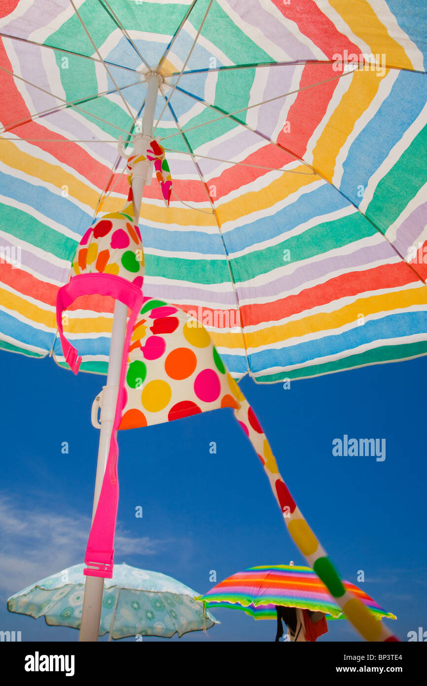 Polka Dot bikini colgando de una colorida sombrilla en una playa soleada Foto de stock