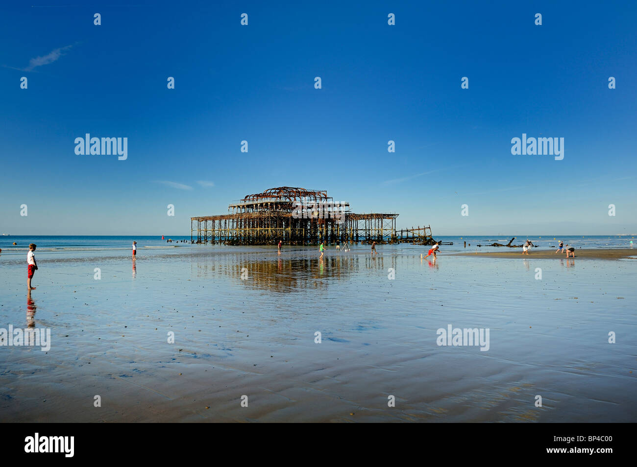 Jugar cricket en marea baja en la playa en frente del Brighton West Pier abandonados Foto de stock